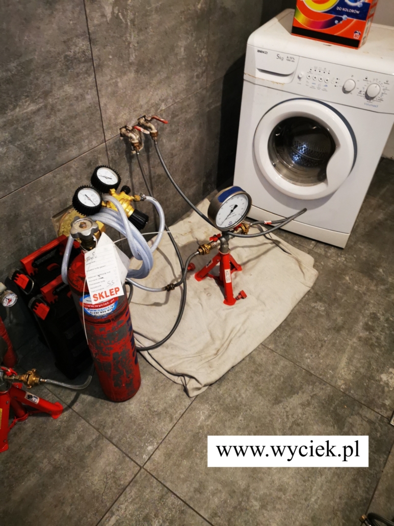 Butla z reduktorem i manometr połączone wężami z instalacją wodną w łazience.